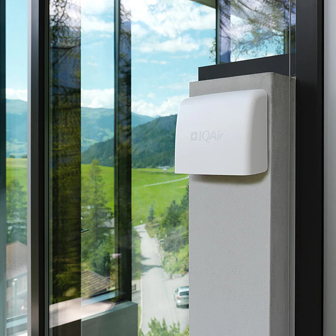 Outdoor air quality monitor mounted on wall near a window overlooking green landscape